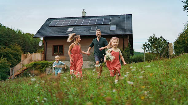 Família a correr no campo, junto de uma casa com paineis fotovoltaicos